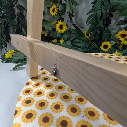 Wooden easel with a sunflower patterned tablecloth against a backdrop of greenery and sunflowers.