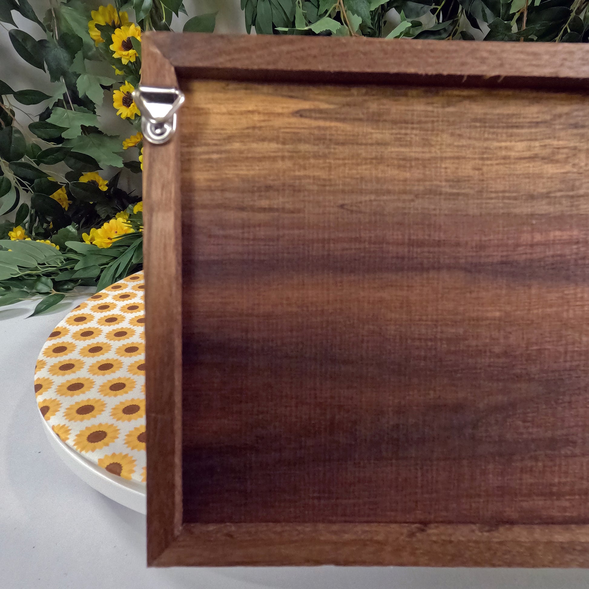 Wooden wall art with a decorative plate featuring sunflower pattern on a white surface with greenery in the background.