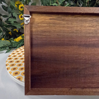 Wooden wall art with a decorative plate featuring sunflower pattern on a white surface with greenery in the background.