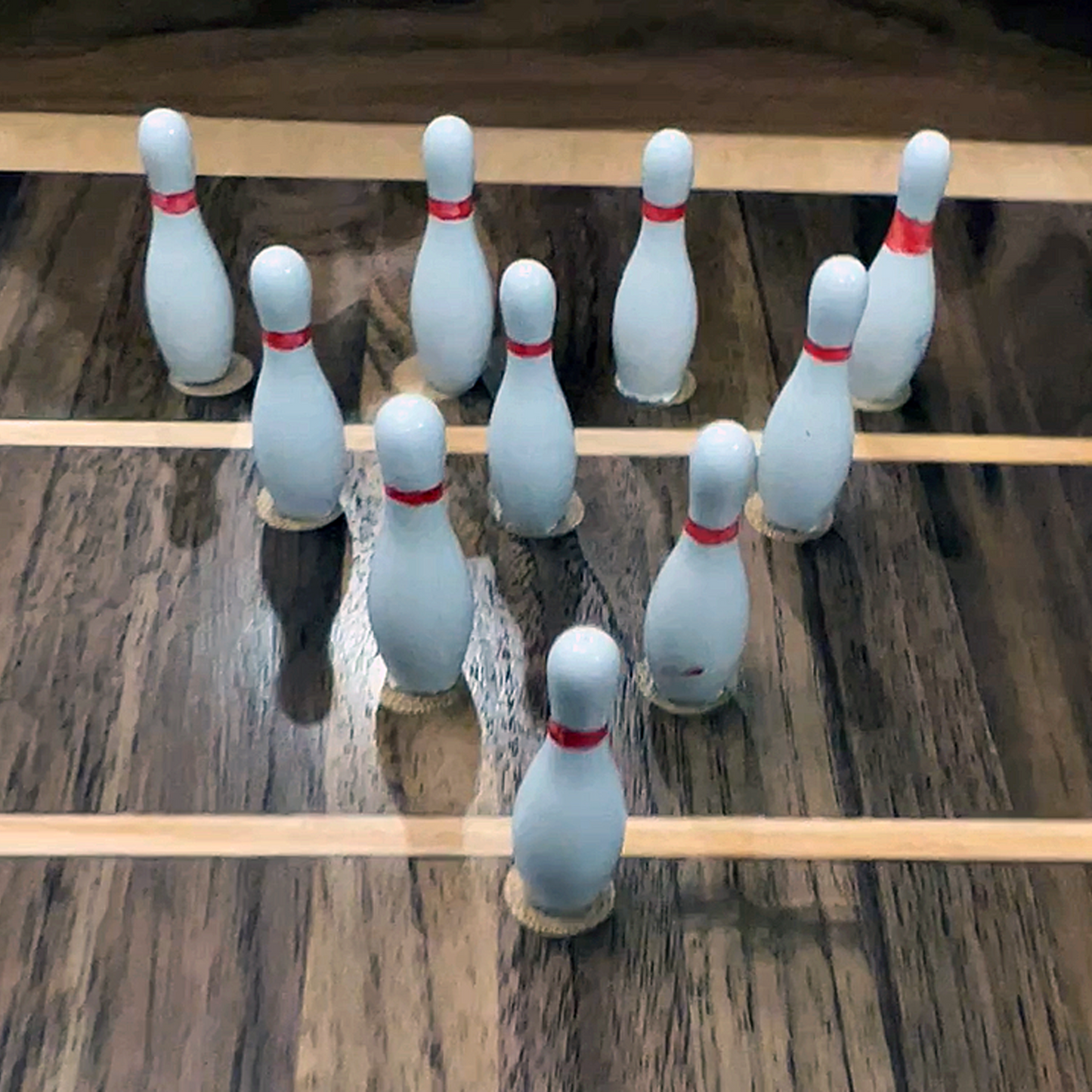 Set of white bowling pins with red bands on a wooden surface