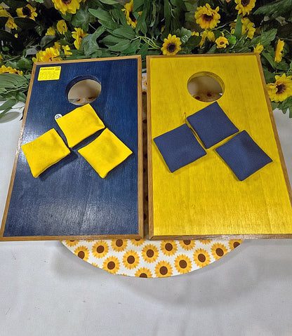 Two cornhole boards with bags on a table with sunflower decorations.
